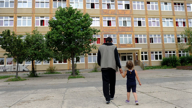 Ariana aus Syrien geht am 30.07.2014 mit einem Verwandten über den Hof in einem Flüchtlingsheim in Berlin-Hellersdorf.