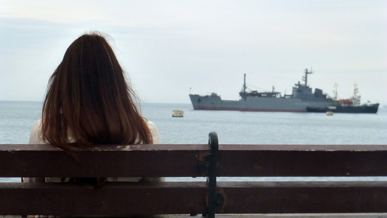 Eine junge Frau schaut am 06.03.2014 vom Ufer der Bucht von Sewastopol auf ein russisches Kriegsschiff.