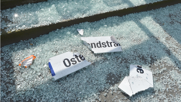 Ein Schild mit der Aufschrift "Ostendstraße" der gleichnamigen Straßenbahn-Haltestelle an der Hanauer Landstraße und Glasscherben liegen am 18.03.2015 in Frankfurt (Hessen) am Rande der offiziellen Eröffnung der Europäischen Zentralbank (EZB) nach Demonstrationen gegen die Eröffnung auf dem Boden.