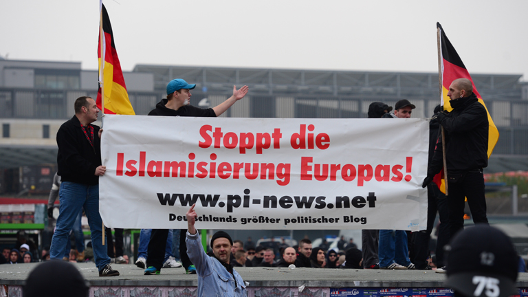 Demonstranten stehen am 15.11.2014 bei der Anti-Islamismus-Demo "Hooligans gegen Salafisten (HoGeSa)" in Hannover (Niedersachsen) und halten ein Plakat mit der Aufschrift "Stoppt die Islamisierung Europas!".