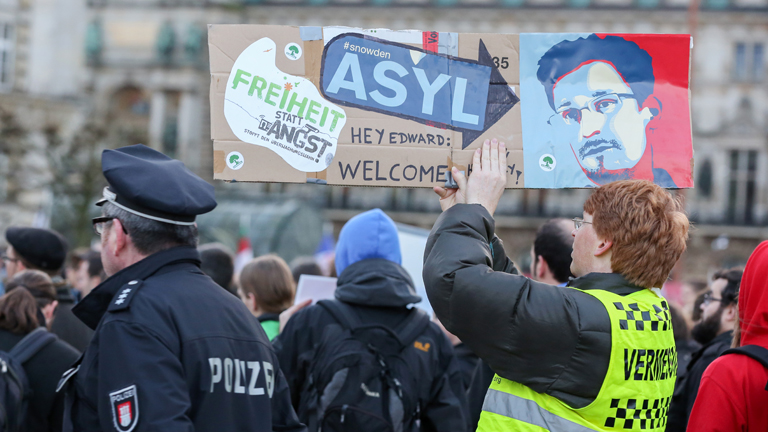 Ein Demonstrant hält bei einer Demonstration ein Plakat mit dem Bildnis Edward Snowdens in die Höhe