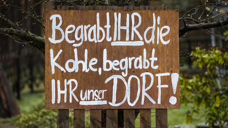 Schild auf dem steht. "Begrabt ihr die Kohle, begrabt ihr unser Dorf!"