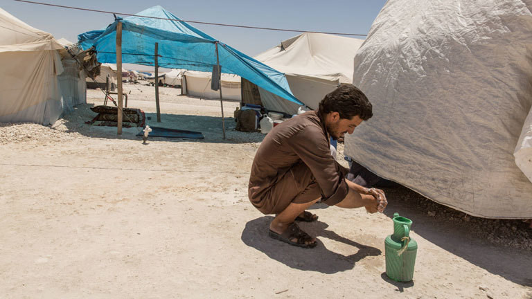 Ein Mann kniet in einem syrischen Flüchtlingscamp am Boden und wäscht sich die Hände.