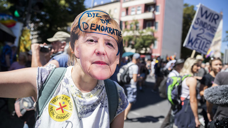 Frau mit Merkelmaske und dem Schriftzug "Bye Bye, Demokratie"