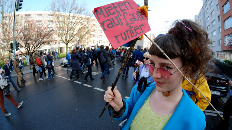 Frau bei einer Demo mit dem Schild "Mieten rauf, Laune runter".
