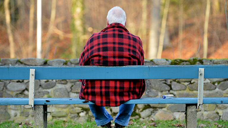Ansicht von hinten: Ein älterer Mann sitzt auf einer Parkbank