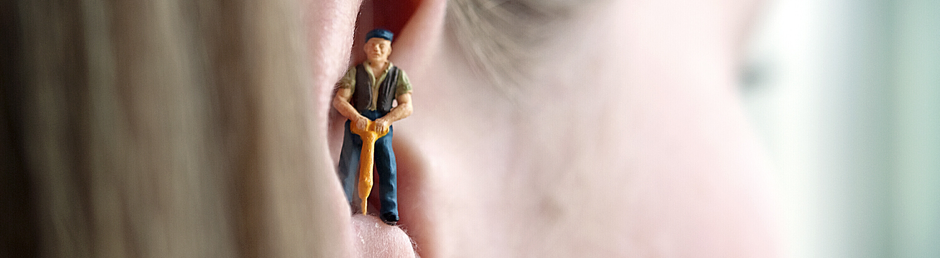 Eine Miniaturfigur eines Bauarbeiters mit Schlagbohrer steht im Ohr einer Frau