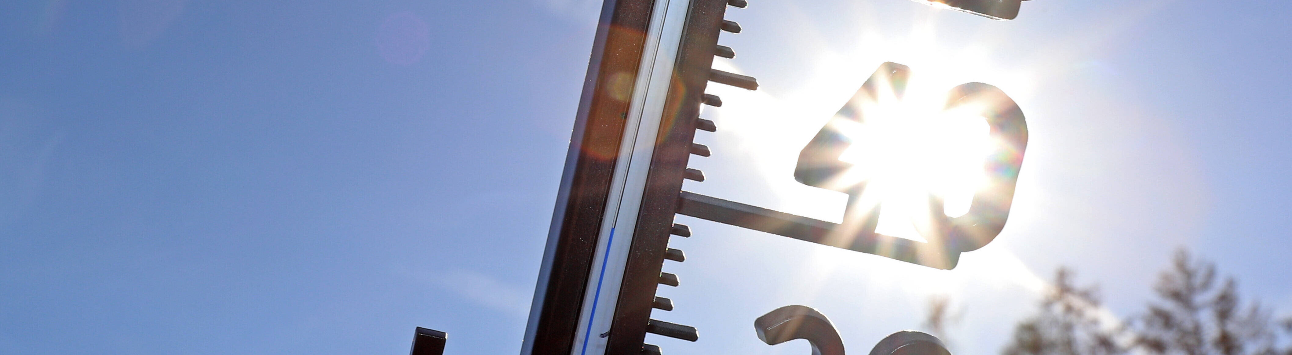 Symbolbild: Ein Thermometer vor blauem Himmel und der Sonne