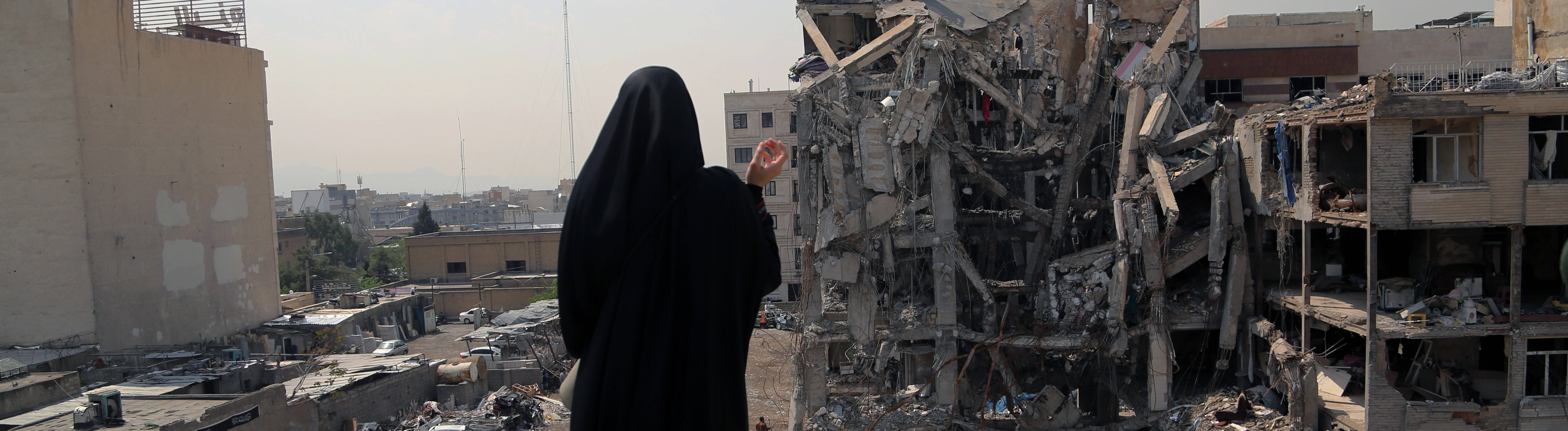 Frau blickt auf zerstörtes Haus in Iran.