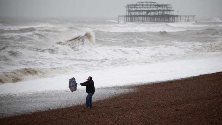 Eine Urlauberin kämpft am Strand des britischen Seebads Brighton mit dem Wind und ihrem Schirm
