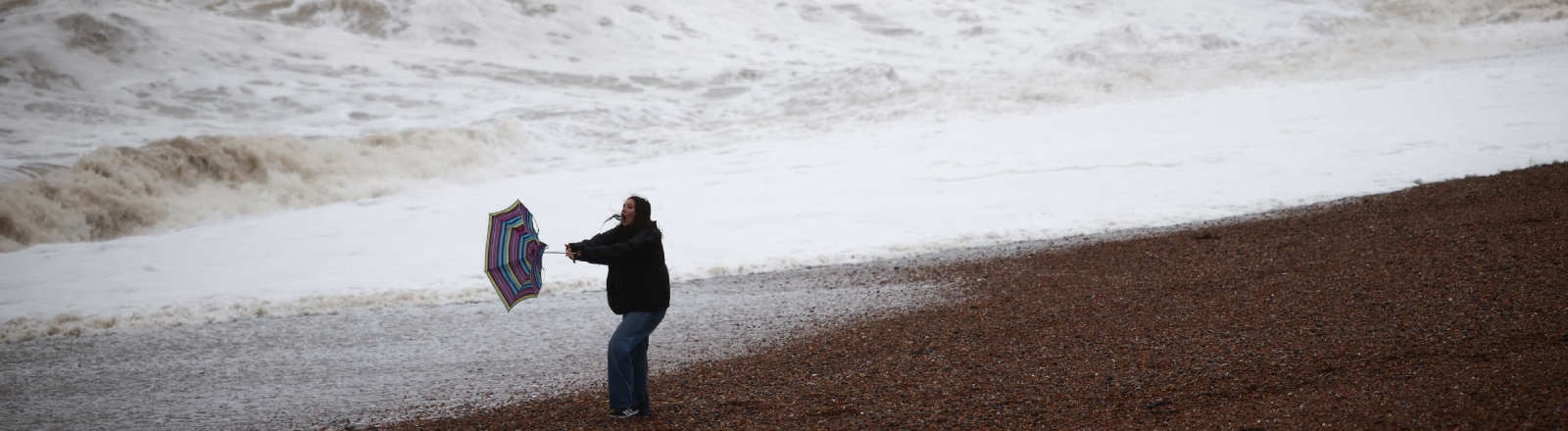 Eine Urlauberin kämpft am Strand des britischen Seebads Brighton mit dem Wind und ihrem Schirm