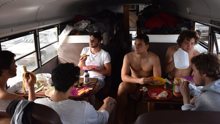 Junge Männer frühstücken gemeinsam in einem umgebauten Schulbus