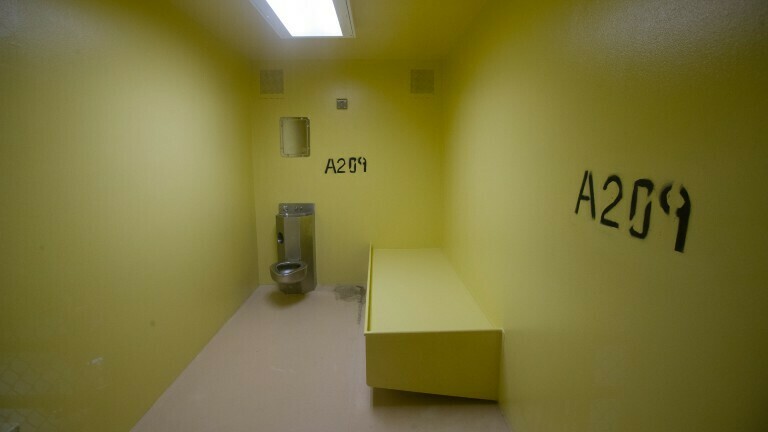Eine leere Zelle – mit gelben Wänden, einer Toilette und einer Pritsche – im Militärgefängnis in Guantánamo