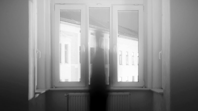 Eine schemenhafte Figur ist an einem Fenster zu erkennen.