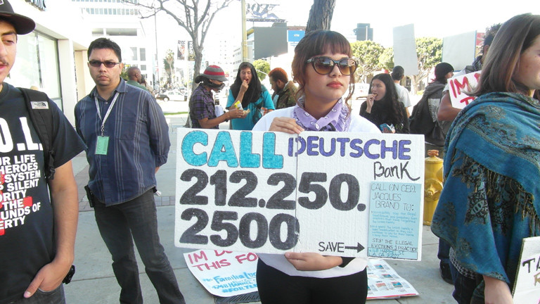 Eine Frau hält ein Protestplakat gegen die Deutsche Bank hoch.
