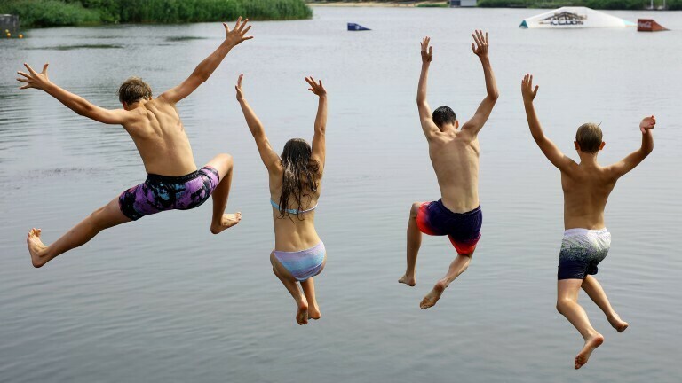 Vier Jugendliche springen in einen See.