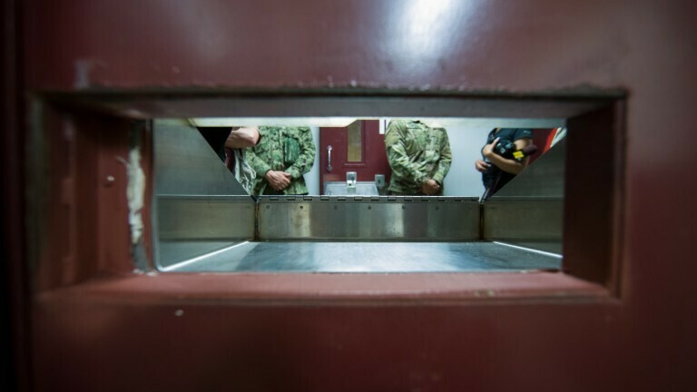Foto durch einen Guckschlitz im Gefängnis in Guantánamo. Auf der anderen Seite sind die Körper von drei Soldaten zu sehen.