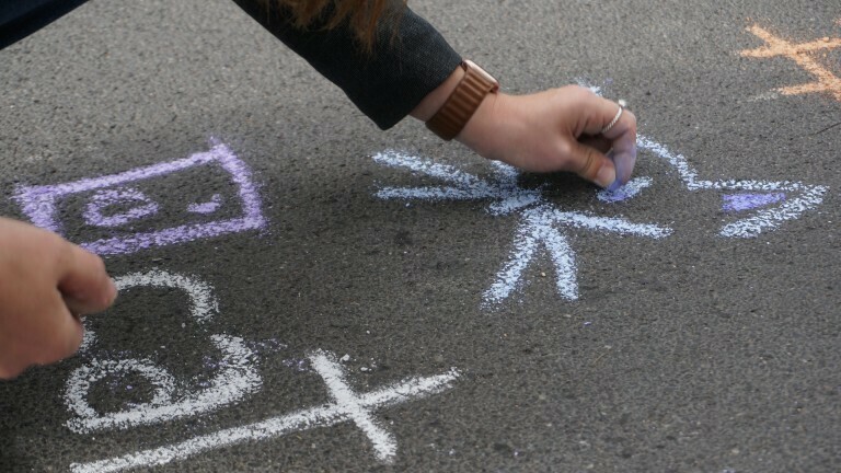 Hand, die mit Kreide auf einer Straße schreibt
