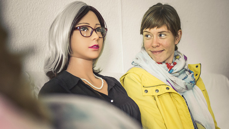 Deutschlandfunk-Nova-Autorin Nora (rechts) ist fasziniert von den Puppen. Auf der Couch fühlt sie sich neben den Damen aus Plastik aber auch ein bisschen unwohl.