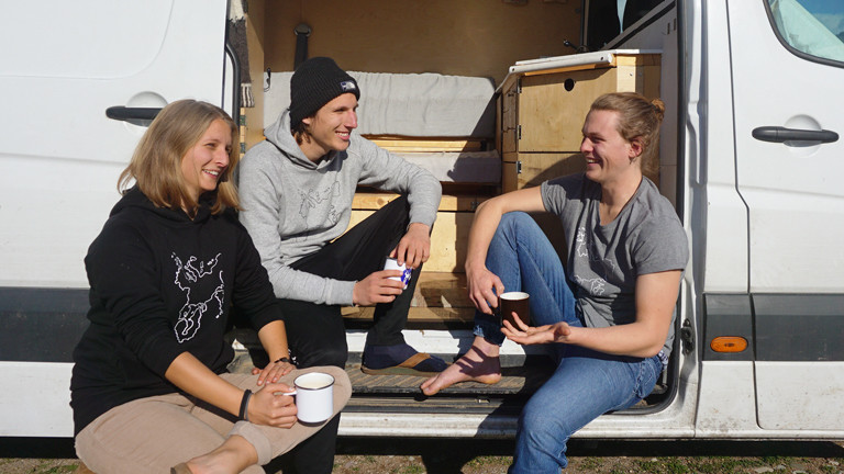 Ina Bierfreund, Felix Hartge und Tim Noetzel trinken Kaffee im Buseingang