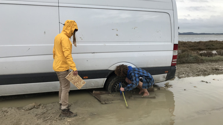 Der Campingbus steckt im Schlamm fest. Ina Bierfreund und ein Helfer versuchen, ihn zu befreien.