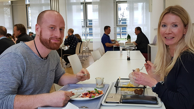 Zwei Menschen sitzen sich beim Mittagessen in der Kantine gegenüber.