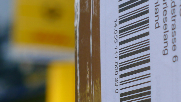 Paketaufkleber und im Hintergrund verschwommen gelb das Schild einer Post.