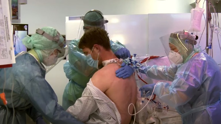 Drei Pflegekräfte setzen einen Corona Patienten in einem Lehrvideo auf