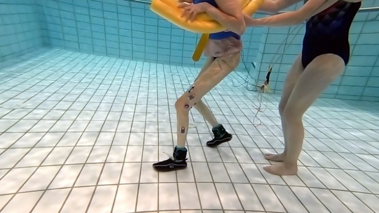 Eine Frau läuft mit Elektroden an den Beinen durchs Wasser