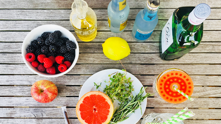 Die Zutaten für einen Gin Tonic mit Grapefruit und Thymiansirup und einen Brombeer-Vanille-Mocktail auf einem Gartentisch