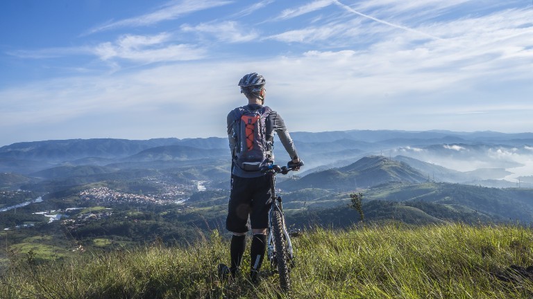 Ein Mann steht mit seinem Rad auf dem Berg und schaut auf ein Tal