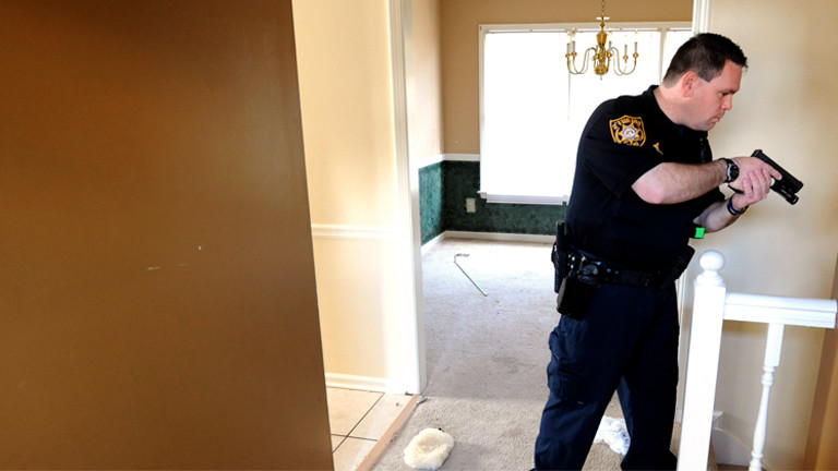 Ein Polizist hält in einem Haus, das gerade zwangsgeräumt wird, eine Waffe in seinen Händen und sucht nach Hausbewohnern.