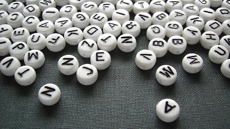 Weiße Spielsteine mit schwarzen Buchstaben liegen auf einem schwarzen Untergrund