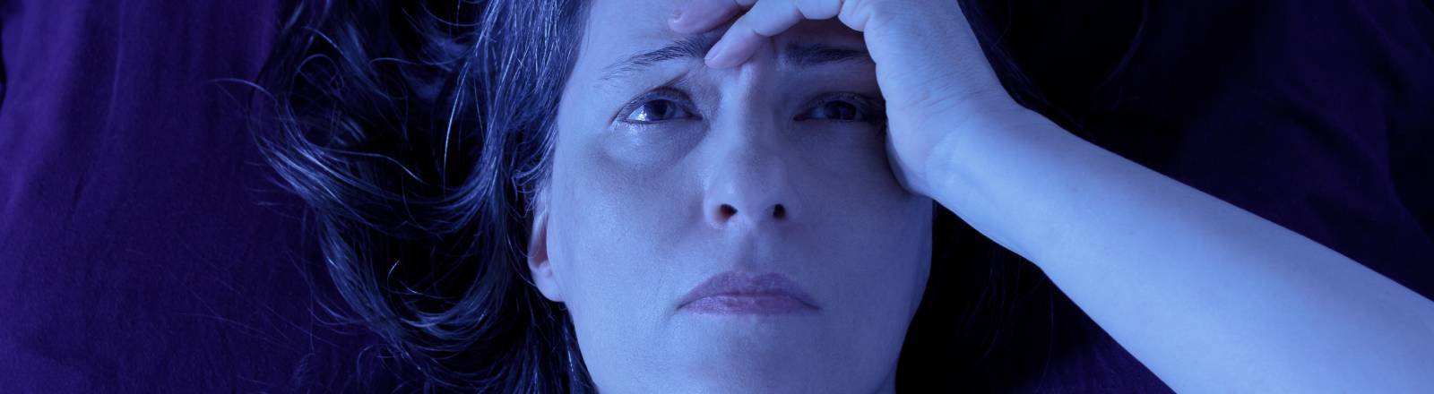 Frau liegt nachts wach grübelnd im Bett.