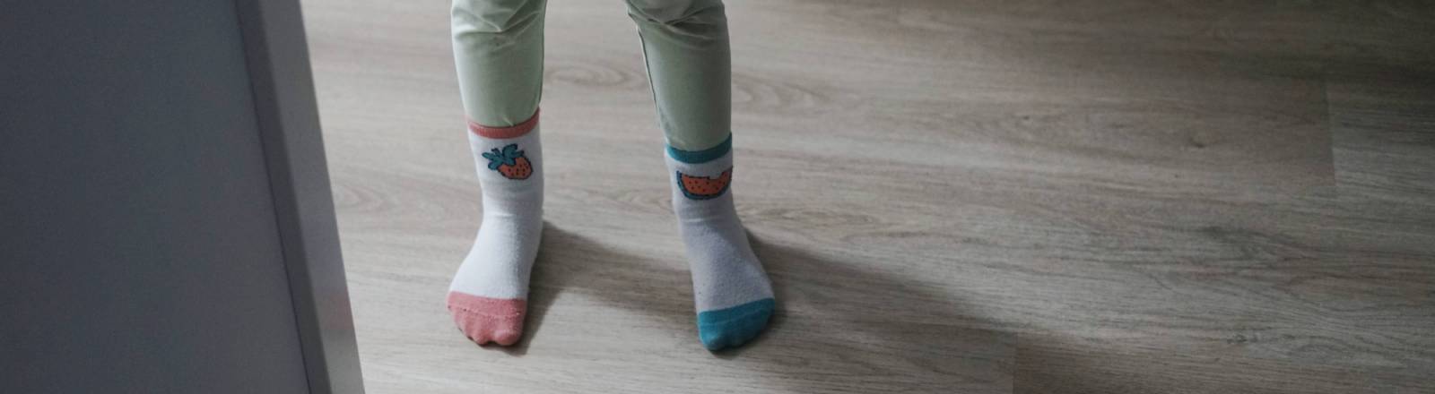 Ein kleines Mädchen, das verschiedene Socken trägt. steht an der Tür zwischen Flur und Schlafzimmer.