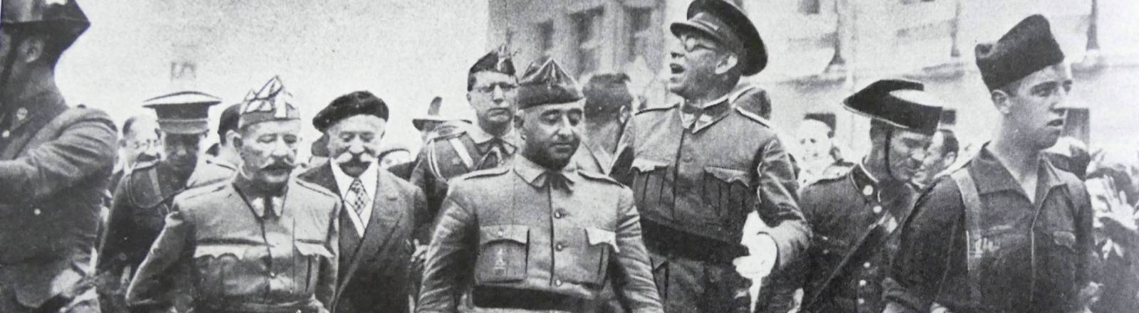 Schwarz-Weiß-Fotografie aus dem August 1936: General Francisco Franco schreitet in Burgos flankiert von den Generälen Emilio Mola, Miguel Cabanellas und José Cavalcanti durch eine Straße.
