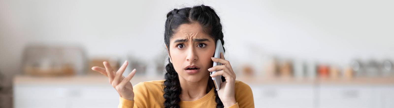 Eine Frau sitzt auf dem Sofa im Wohnzimmer und telefoniert mit einem Scam-Anrufer.