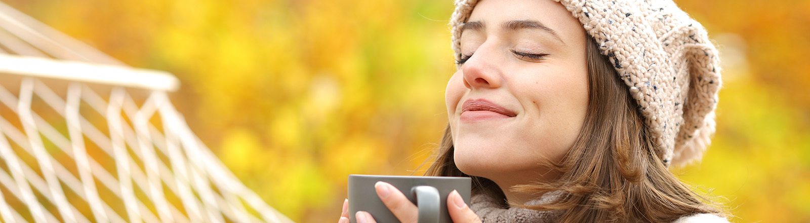 Eine Frau steht im Frühling im Wald und atmet verschiedene Düfte ein. Sie hält in der Hand eine Tasse