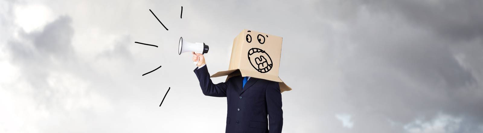 Ein Symbolbild eines verärgerten Geschäftsmanns. Er hält eine Flüstertüte in der Hand und trägt einen Karton auf dem Kopf.