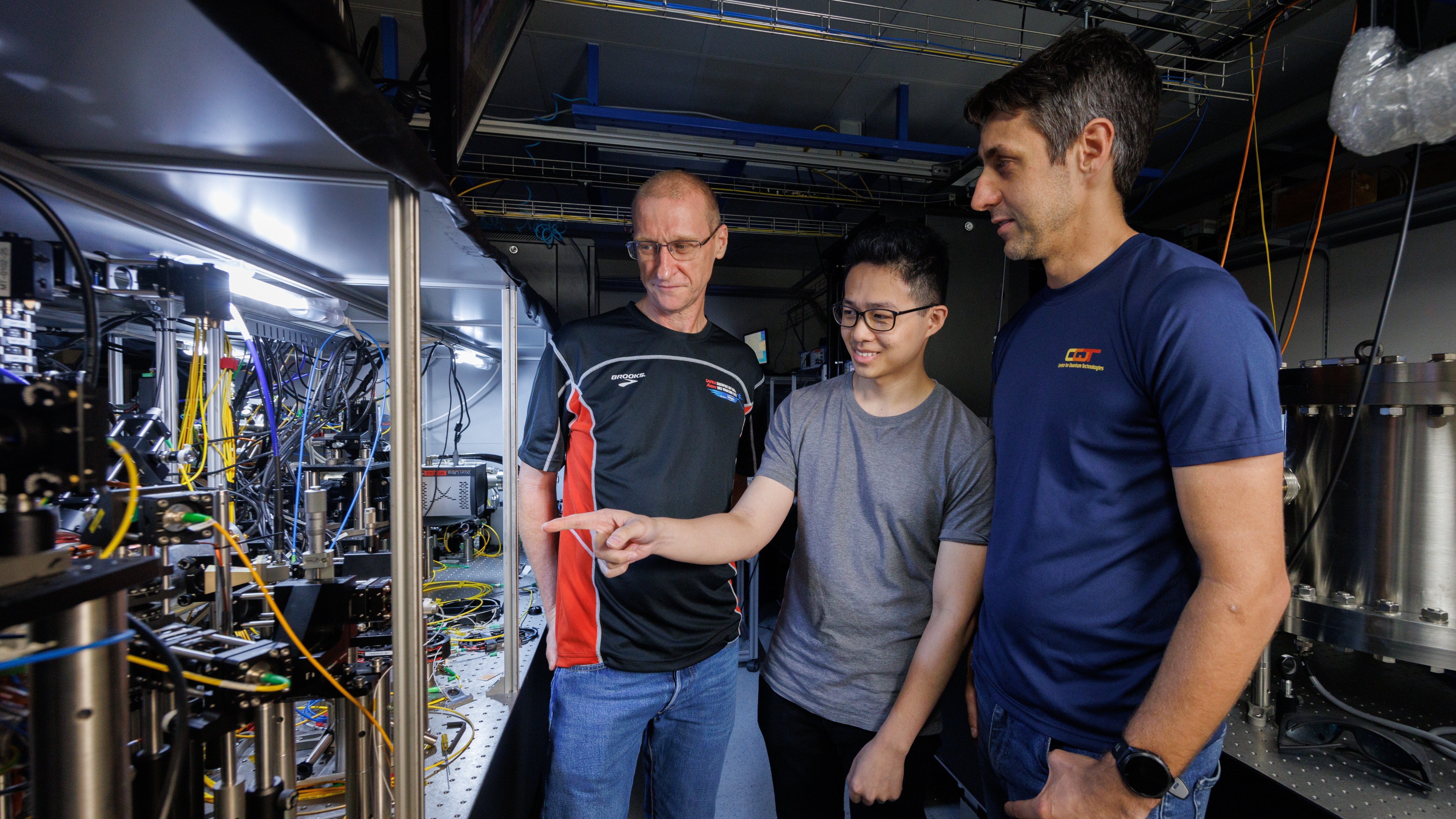 Die Forscher Murray Barrett, Michael Lee und Kyle Arnold zeigen auf die Atomuhr
