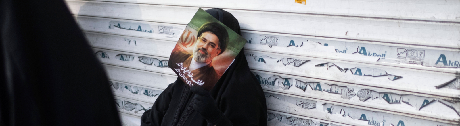 Eine verschleierte Iranerin lehnt sich während einer Jubeldemonstration für Mojtaba Khamenei Anfang März 2026 an die Jalousie eines Geschäfts.