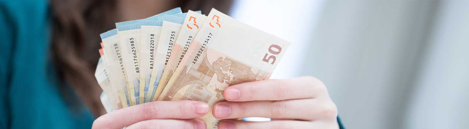 Foto der Hände einer jungen Frau, die Euro-Scheine aufgefächert in der Hand hält