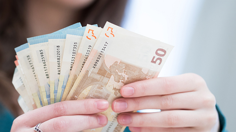 Foto der Hände einer jungen Frau, die Euro-Scheine aufgefächert in der Hand hält