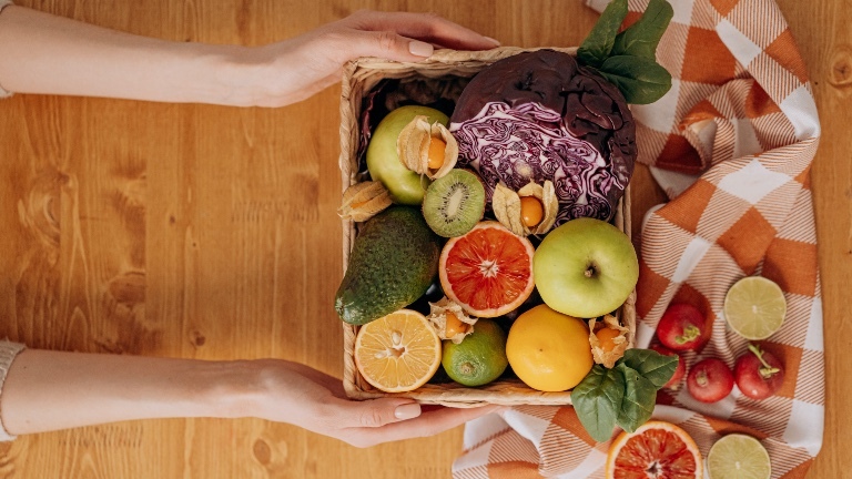 Eine Person hält einen Korb mit Gemüse und Obst zwischen den Händen