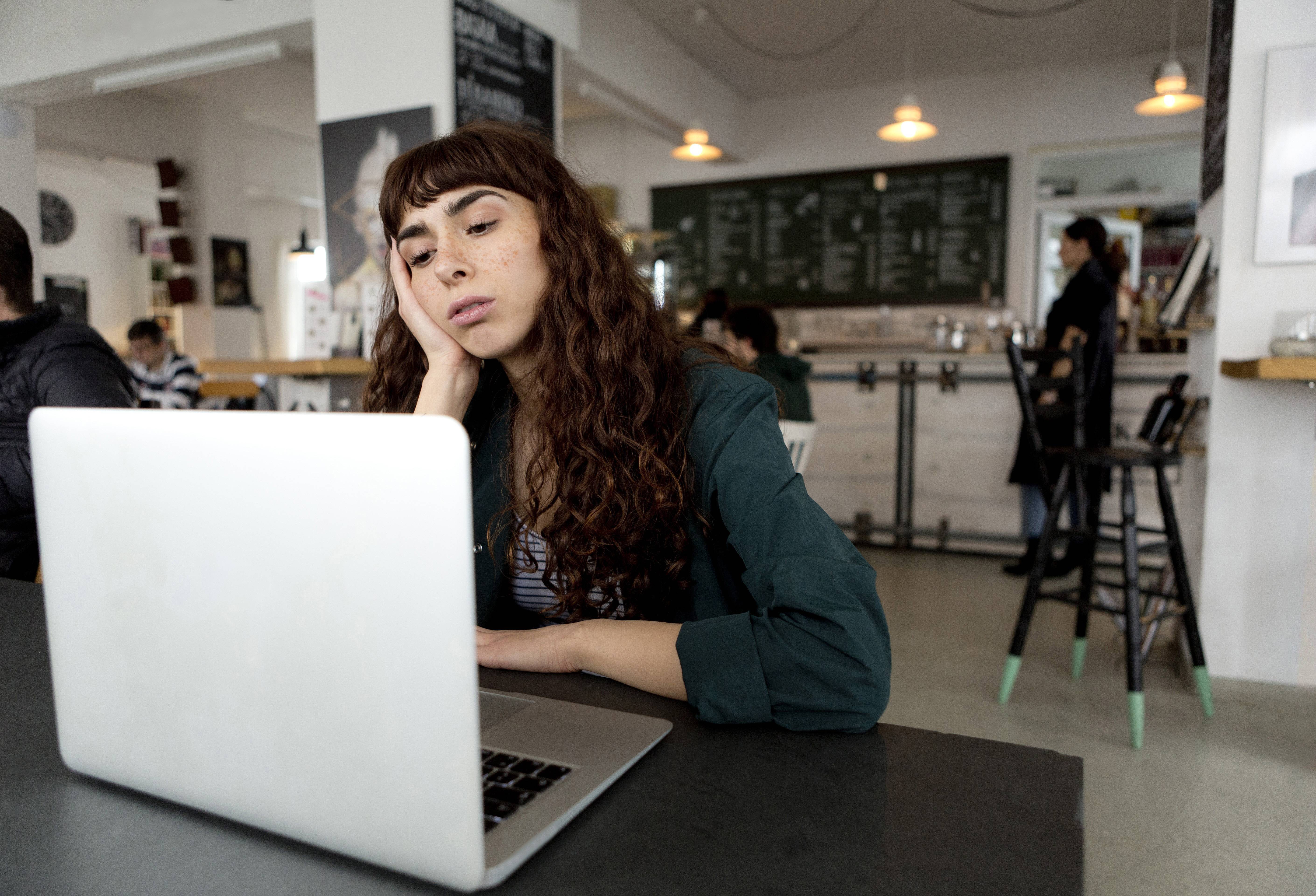 Studentin in Cafe schaut genervt auf Laptop, könnte an langen Ladezeiten liegen