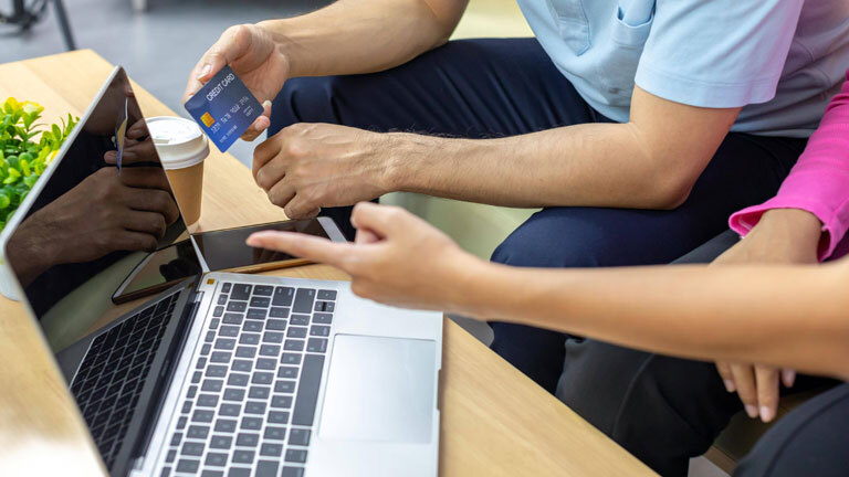 Ein Mann und eine Frau sitzen vor einem Laptop. Er hält eine Kreditkarte in der Hand.