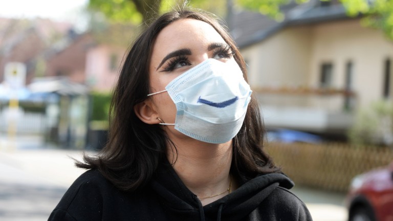 Eine junge Frau mit Maske und einem lächelnden Mundwinkel darauf