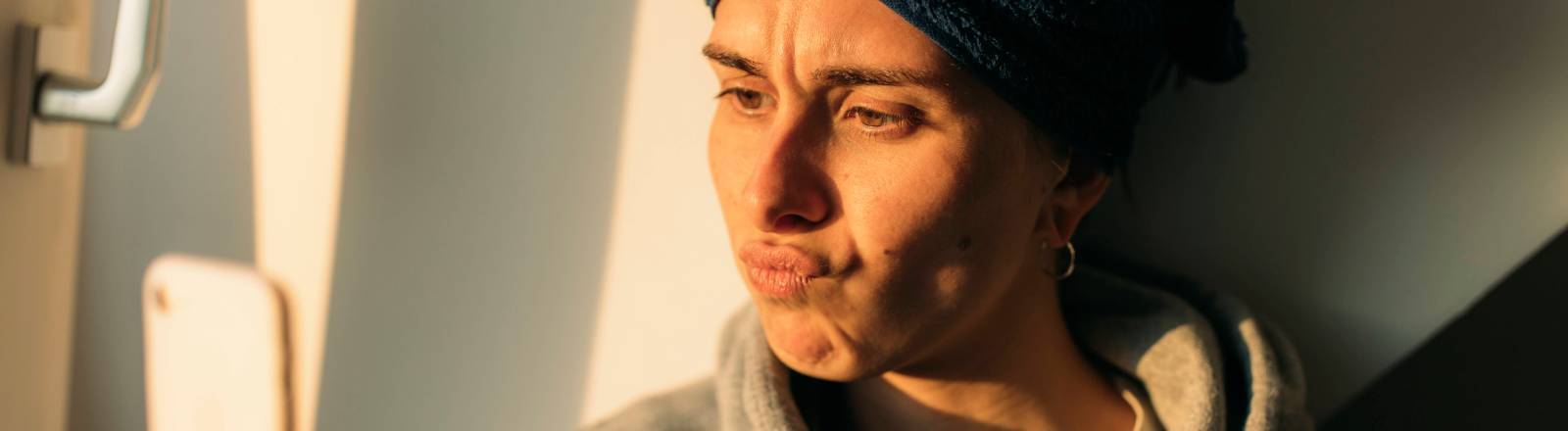 Frau mit Handtuchturban schaut frustriert aufs Smartphone.