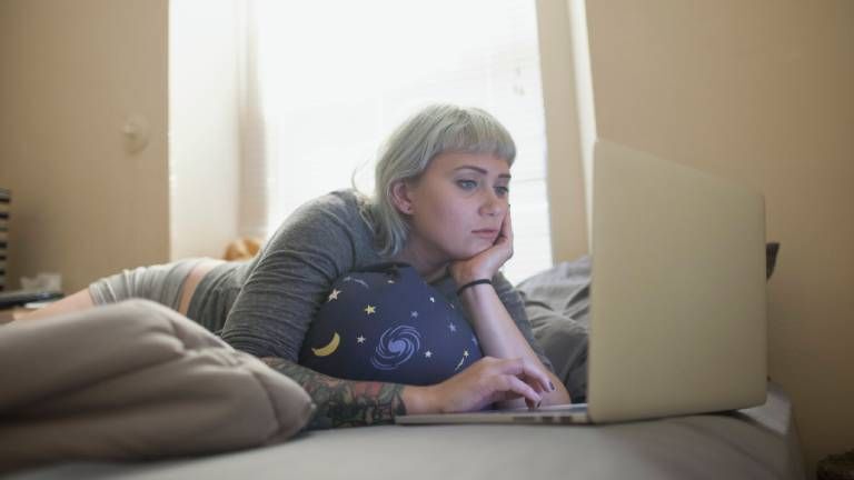 Eine Frau liegt auf dem Sofa und ist am Laptop.