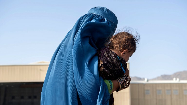 Eine Frau in Afghanistan, die Burka trägt und ein Kleinkind auf dem Arm hält.